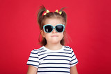 Cute little girl in sunglasses on red background