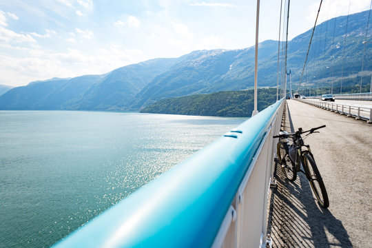 Theme of mountain biking in Scandinavia. human tourist in helmet and sportswear on bicycle in Norway on Hardanger Bridge suspension bridge thrown across the Hardanger Fjord in southwestern Norway