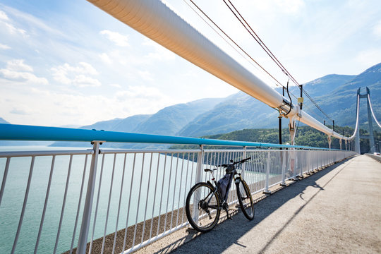 Theme of mountain biking in Scandinavia. human tourist in helmet and sportswear on bicycle in Norway on Hardanger Bridge suspension bridge thrown across the Hardanger Fjord in southwestern Norway