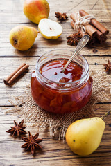 Homemade pear jam in a jar and fresh pears on a wooden background.