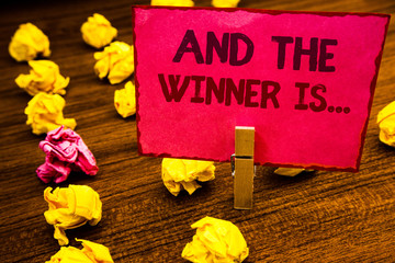 Fototapeta premium Conceptual hand writing showing And The Winner Is . Business photo showcasing Announcing as first place in competition or race Paperclip retrain pink card with letters wooden floor hunch
