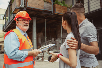 Foreman or achitect engineer shows future house, office or store design plans to a young couple....
