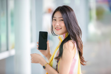 Young and beautiful Asian woman with colourful shopping bag holding her mobile phone while shopping in the shopping mall.