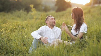 A young couple is sitting on a bright green meadow. Couple in love. Smiling and having a good time outside on a warm summer day