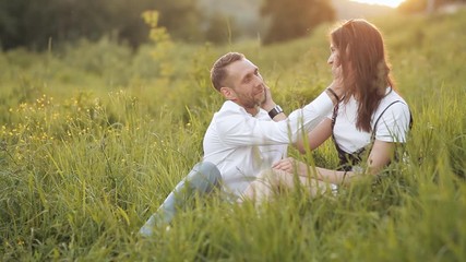 A young couple is sitting on a bright green meadow. Couple in love. Smiling and having a good time outside on a warm summer day