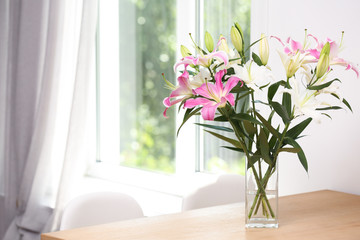 Vase with bouquet of beautiful lilies on wooden table indoors. Space for text