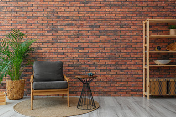 Fototapeta na wymiar Modern room interior with stylish grey armchair and potted plant near brick wall