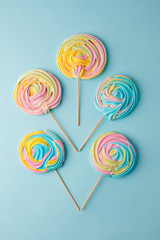 Colorful unicorn rainbow color meringue lollipops candy on pale on blue background. Flat lay. Summer sweet abstract Minimal concept.