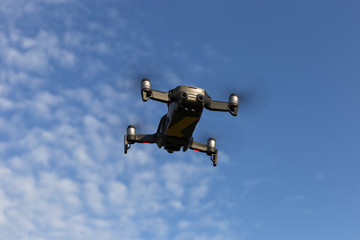A drone, a quadrocopter with a camera for video shooting, flies against a blue sky with clouds.