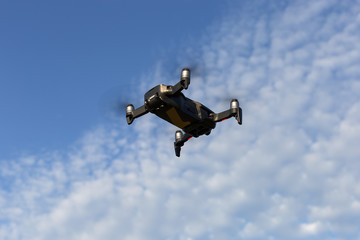 A drone, a quadrocopter with a camera for video shooting, flies against a blue sky with clouds.