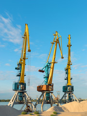 Cranes near the sand against a blue sky. Industrial landscape, industrial zone.
