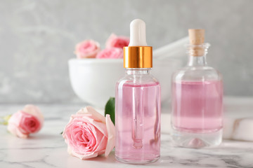 Fototapeta na wymiar Bottle of essential oil and rose on marble table