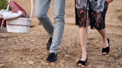 A young couple walks at sunset on a summer day, on a green meadow. Picnic in nature, basket with wine and food and a plaid