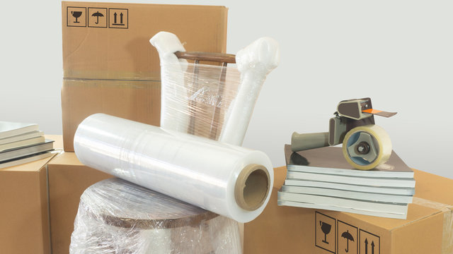 Moving scene with a roll of plastic to pack on a chair wrapped in plastic with closed cardboard boxes, books and masking tape on white background