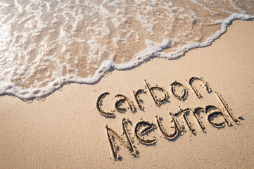 Fototapeta premium Carbon Neutral message handwritten on smooth sand beach with incoming wave