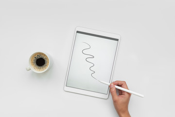 Cup of coffee and feminine hands drawing on tablet by pencil on white desk. Top view. Copy space. Mock-up