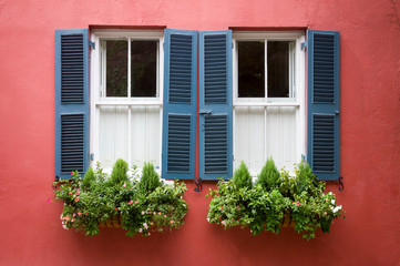 Fototapeta na wymiar Scenic summer detail of window boxes filled with summer greenery decorating a traditional old Georgian colonial building with blue shutters in Charleston, South Carolina, USA