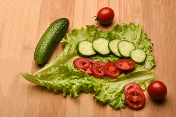 Fresh cucumbers, tomatoes and lettuce on a wooden background.