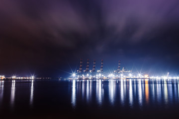 Guindastes em um porto vistos durante a noite, com reflexos das luzes no mar