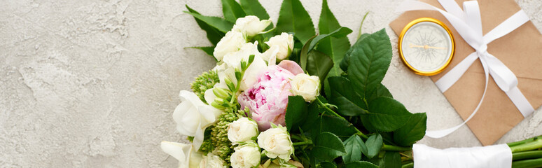 panoramic shot of bouquet near golden compass and envelope with white ribbon on textured surface