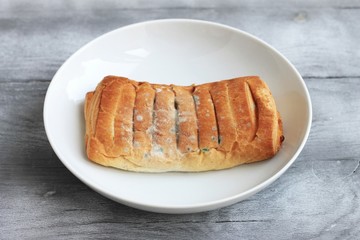 Moldy inedible spoiled food. Pasty with mold in a white plate on a gray background.