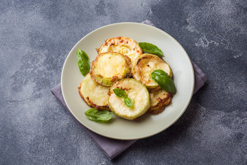 Slices of fried zucchini in batter with garlic and Basil on a plate.