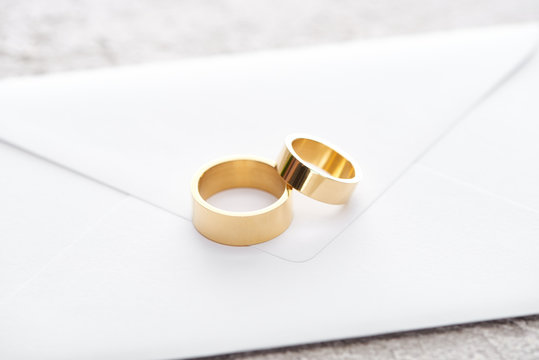 golden wedding rings on white envelope on grey textured surface