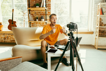Young caucasian male blogger with professional camera recording video review of gadgets at home. Blogging, videoblog, vlogging. Man making vlog or live stream about photo or technical novelty.