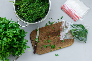 Disposable package with chopped fresh green parsley and dill or fennel on gray wooden table. Top view. Copy space. Harvesting concept