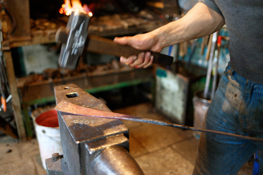 Blacksmith forging red-hot metal with hammer.