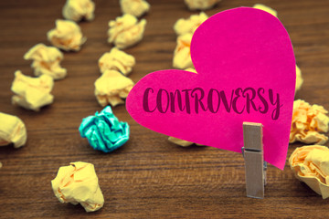 Word writing text Controversy. Business concept for Disagreement or Argument about something important to people Clothespin holding pink heart paper crumpled papers ideas mistakes trials