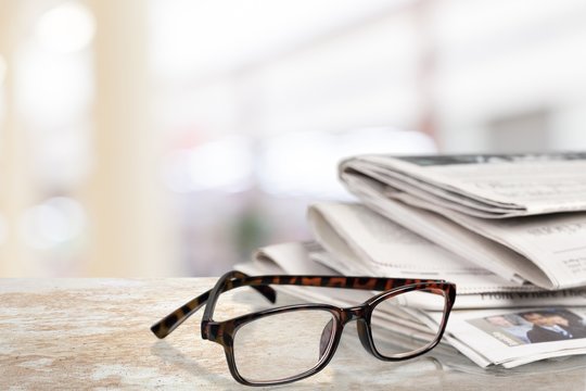 Newspapers with reading glasses on background