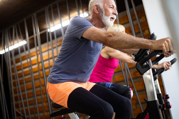 Happy fit mature woman and man cycling on exercise bikes to stay healthy