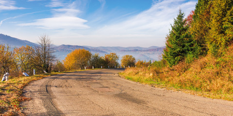 old serpentine road in mountains. beautiful autumn scenery in morning misty light. wonderful october weather with fluffy clouds on the sky. ridge in the distance