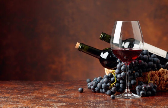 Juicy blue grapes and bottles of red wine on a brown background.