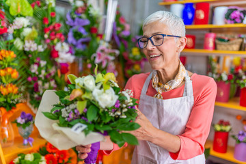 Smiling portrait of an attractive florist business woman owner at a flower shop market working and making a new floral arrangement during a sunny day. Small business owner.