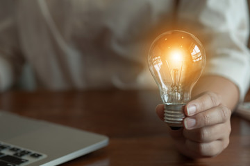 woman hands holding light bulb in working place.