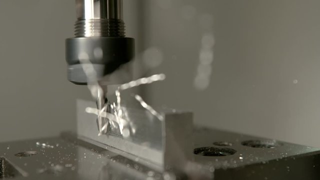 SLOW MOTION, MACRO, DOF: Twisted aluminium shavings come flying off a workpiece during end milling. Sharp cutter spinning and shaving the side of a block of aluminium. Conventional metalwork method.