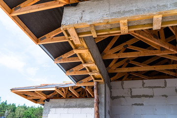 Obraz premium Roof trusses covered with a membrane on a detached house under construction, visible roof elements, battens, counter battens, rafters.