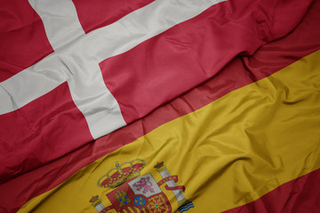 waving colorful flag of spain and national flag of denmark.