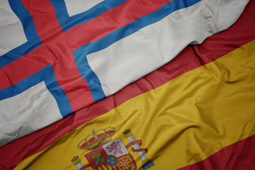 waving colorful flag of spain and national flag of faroe islands.