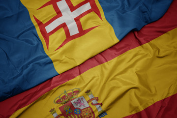 waving colorful flag of spain and national flag of madeira.