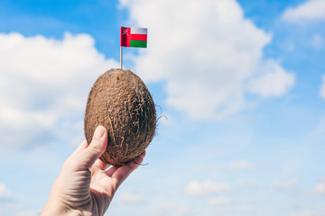 Tropical coconut with Omani flag in the form of a toothpick in female hands. Tourism in Oman. concept