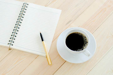 Brown wooden table with laptop notepad pen and a cup of black coffee