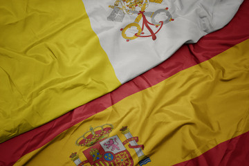 waving colorful flag of spain and national flag of vatican city.
