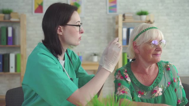 doctor in the clinic helps to put a hearing aid in the ear of elderly woman close up
