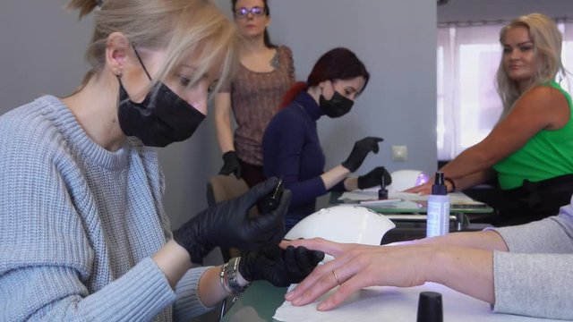 Student of manicure courses concentrates on gel coating. Teacher observes from afar