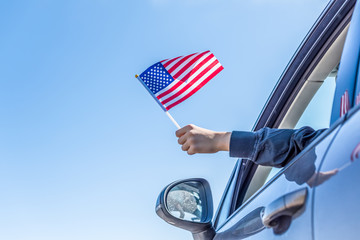 Boy holding Flag of America from the open car window on the sky background. USA.Concept