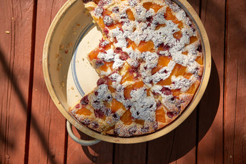 Close-up overhead homemade apricot and cherries pie in rustic ceramic form on red painted wooden board. 