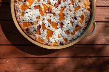 Overhead homemade fruit pie in rustic ceramic form on red painted wooden board
